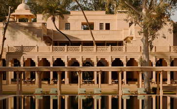 Amanbagh's main building reflected in the pool, with arched colonnades and warm stone architecture framed by trees.