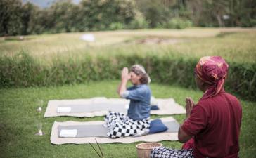 Two people seated on a picnic blanket at Amanjiwo, with one in a pink hat and the other in burgundy, overlooking green fields.