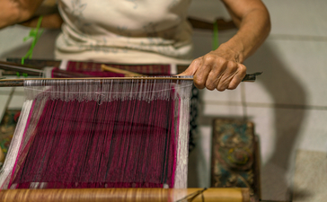 Artisan weaving traditional textile on wooden loom at Amankila resort, Bali.