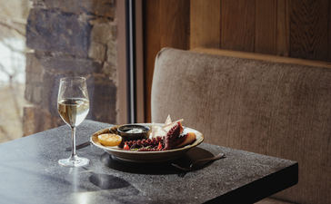 Dining table at Amangani with white wine glass and bowl of appetisers beside a window.
