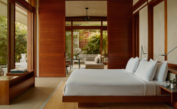 Casita bedroom at Amanera resort with terracotta walls, wooden bed and garden views through floor-to-ceiling windows.