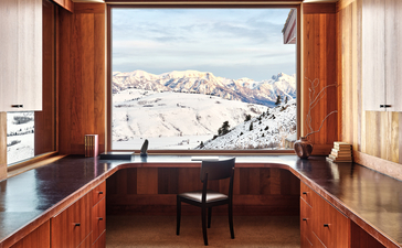 Wooden desk and chair facing open doors with snow-capped mountain views at Amangani, USA.