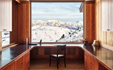 Wooden desk and chair facing open doors with snow-capped mountain views at Amangani, USA.