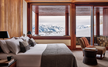 Amangani principal bedroom with snow-capped mountain views through large wooden-framed windows.