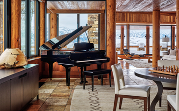 Grand piano in the West Tatanka House at Amangani, with mountain views through timber-framed windows.