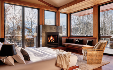 Principal bedroom at Amangani with fireplace and winter forest views through large windows.