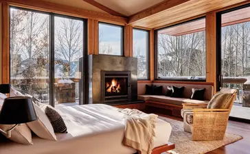 Principal bedroom at Amangani with fireplace and winter forest views through large windows.