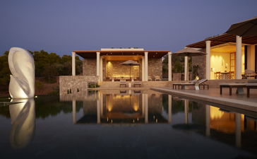 Villa illuminated at dusk with reflection in still water, Amanzoe resort, Greece.