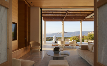 Villa bedroom at Amanzoe resort with panoramic windows framing Aegean Sea views and terrace beyond.