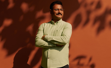 Aman-i-Khas General Manager Aman stands against a terracotta wall, arms crossed, with dappled shadows cast across the surface.
