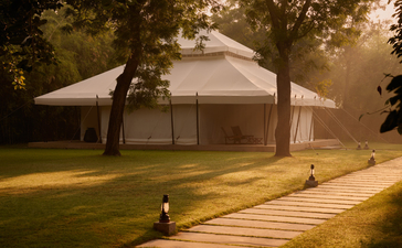 Wooden deck leading towards a canvas tent at Aman-i-Khas at dusk, surrounded by trees.