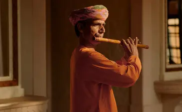 Musician playing traditional instrument at Amanbagh, dressed in rust-coloured robes.