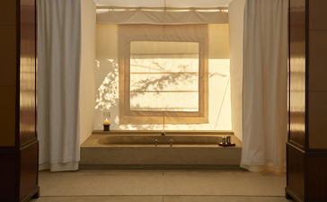 Bathtub positioned beneath a window with golden-hued frame and curtains in a tent accommodation at Aman-i-Khas, India.