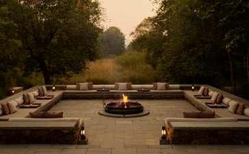 Symmetrical dining pavilion at Aman-i-Khas with central fire pit, stone seating, and tree-lined avenue at dusk.