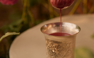Hand holding a rose petal above a glass of water at Aman-i-Khas, India.