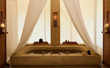 Spa bath at Aman-i-Khas with sunken wooden tub and sheer curtains framing tall windows.