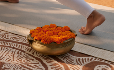 Yoga practitioner's bare feet beside a bowl of marigold petals during a wellness ritual at Aman-i-Khas, India.