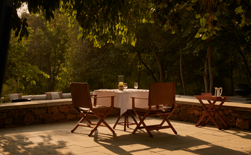 Outdoor dining setup at Aman-i-Khas with wooden table and chairs beneath trees at dusk.