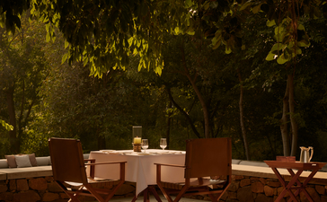 Outdoor dining area at Aman-i-Khas with a table and chairs beneath dappled tree shade.