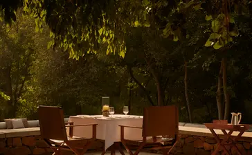 Outdoor dining area at Aman-i-Khas with a table and chairs beneath dappled tree shade.