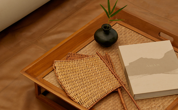 Wooden tray with woven details, small plant and open book inside an Aman-i-Khas tent.