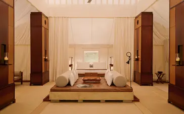 Spacious tent living area at Aman-i-Khas with symmetrical wooden furnishings, central seating platform, and warm ambient lighting.