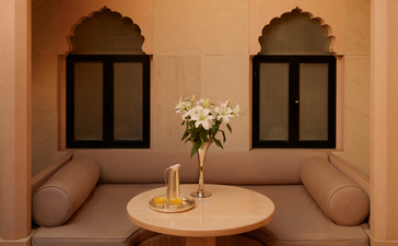 Courtyard alcove at Amanbagh with arched niches, cushioned seating and a round table holding fresh flowers.