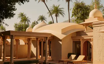 Pool pavilion at Amanbagh with terracotta dome and wooden columns, framed by palm trees.