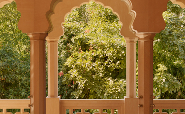 Terrace of Haveli Suite with arched doorway and carved lattice screens overlooking garden at Amanbagh, India.