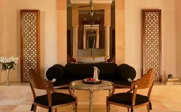 Amanbagh lounge area with two black chairs facing a round table, framed by decorative wooden screens and warm lighting.