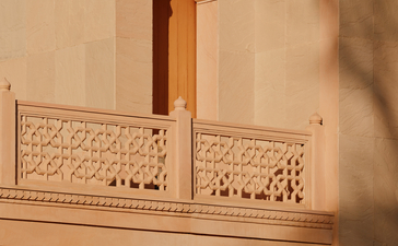 Amanbagh's main building exterior detail showing carved stone balcony with decorative lattice work and traditional architectural elements.