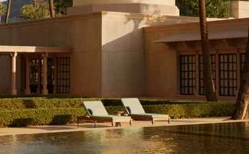 Two loungers on a manicured lawn beside a still pool at Amanbagh, India, with earth-toned pavilions beyond.