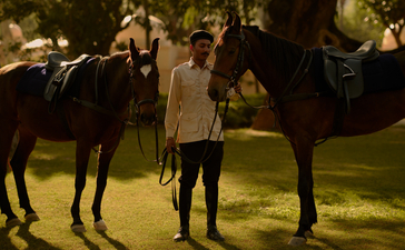 Jockey standing between two horses at Amanbagh at dusk.
