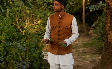 Doctor at Amanbagh wearing traditional terracotta waistcoat and cream robes amid lush garden pathways.