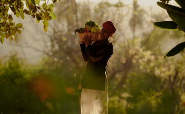 Gardener tending to plants at Amanbagh, framed by morning light and foliage.