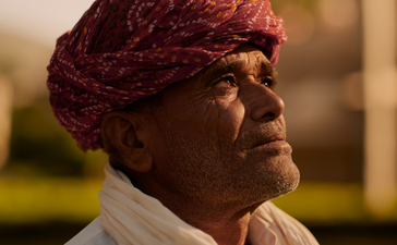Woman wearing burgundy turban and cream scarf at Amanbagh, looking toward distant landscape.