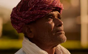 Woman wearing burgundy turban and cream scarf at Amanbagh, looking toward distant landscape.