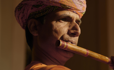Musician playing a wooden wind instrument at Amanbagh, wearing traditional headwrap.