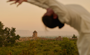 Yoga practice at Amanbagh, with a guest in a forward bend pose overlooking green gardens at dawn.