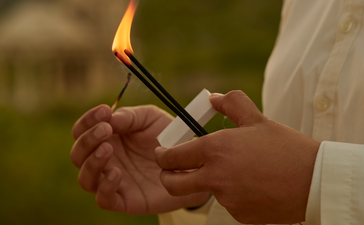 Hands holding a lit incense stick during a yoga session at Amanbagh.