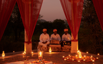 Candlelit chhatri dinner at Amanbagh, with guests seated beneath red drapes and glowing lanterns at dusk.