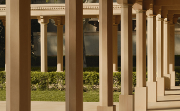 Colonnade walkway at Amanbagh with stone columns casting shadows, opening to gardens beyond.