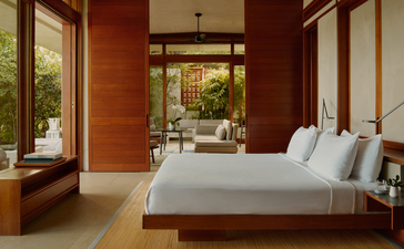 Casita bedroom at Amanera resort with wooden bed, white pillows, and terracotta walls opening to garden views.
