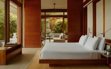 Amanera casita bedroom with terracotta walls, wooden bed frame, and garden views through open doors.