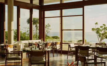 Amanera dining venue with wooden furniture and expansive windows overlooking Dominican landscape.