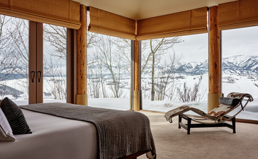 Principal bedroom at Amangani with corner windows overlooking snow-covered Jackson Hole mountains and forest.