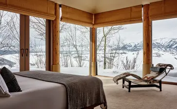 Principal bedroom at Amangani with corner windows overlooking snow-covered Jackson Hole mountains and forest.
