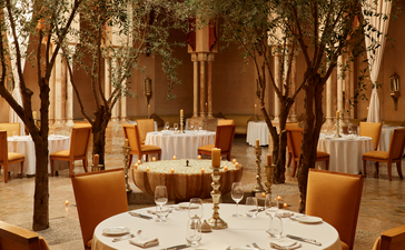 Amanjena's dining venue with ochre-toned walls, tree-lined columns, and a formally set table for fine dining.
