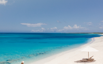 Plage de sable blanc et eaux turquoise à Amanyara resort, avec un voilier traditionnel amarré près du rivage.