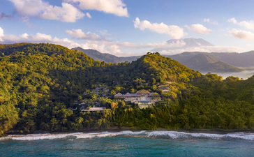 Amankila's clifftop setting overlooks turquoise waters and forested hillsides under clear skies.